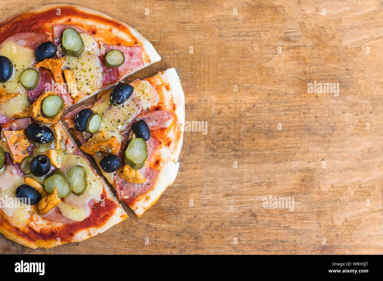 Homemade pizza with tomato sauce, cheese , olives , ham and mushrooms on wooden table. High angle view with space for text Stock Photo