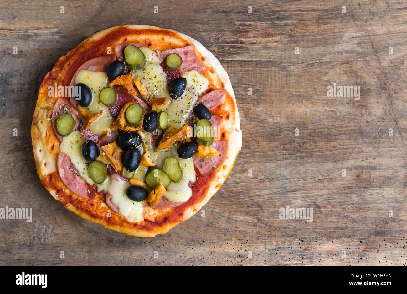 Homemade pizza with tomato sauce, cheese , olives , ham and mushrooms on wooden table. High angle view with space for text Stock Photo