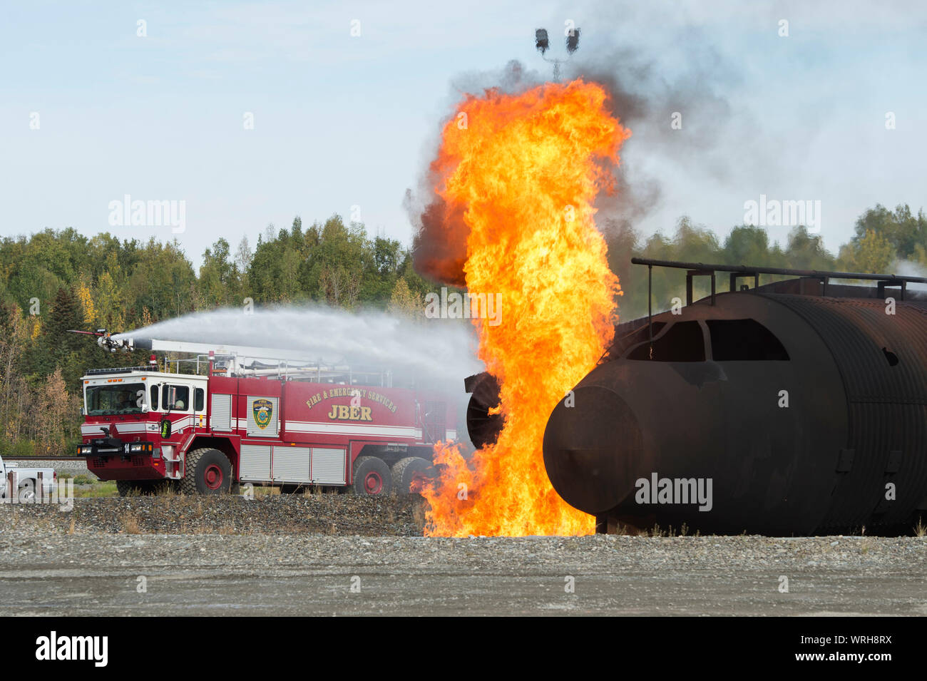 U.S. Air Force fire protection specialists with the 673d Civil Engineer Squadron spray water on a simulated aircraft fire during a fire protection capabilities demonstration at JBER, Alaska, Sept. 6, 2019. Col. Patricia Csànk and Command Chief Master Sgt. Lee Mills, the JBER and 673d Air Base Wing commander and senior enlisted leader, respectively, participated in the demonstration to better understand the physical demands, gear requirements and conditions that might be encountered in an emergency situation. During the demonstration, Csànk and Mills donned fire protection gear, scaled a rescue Stock Photo