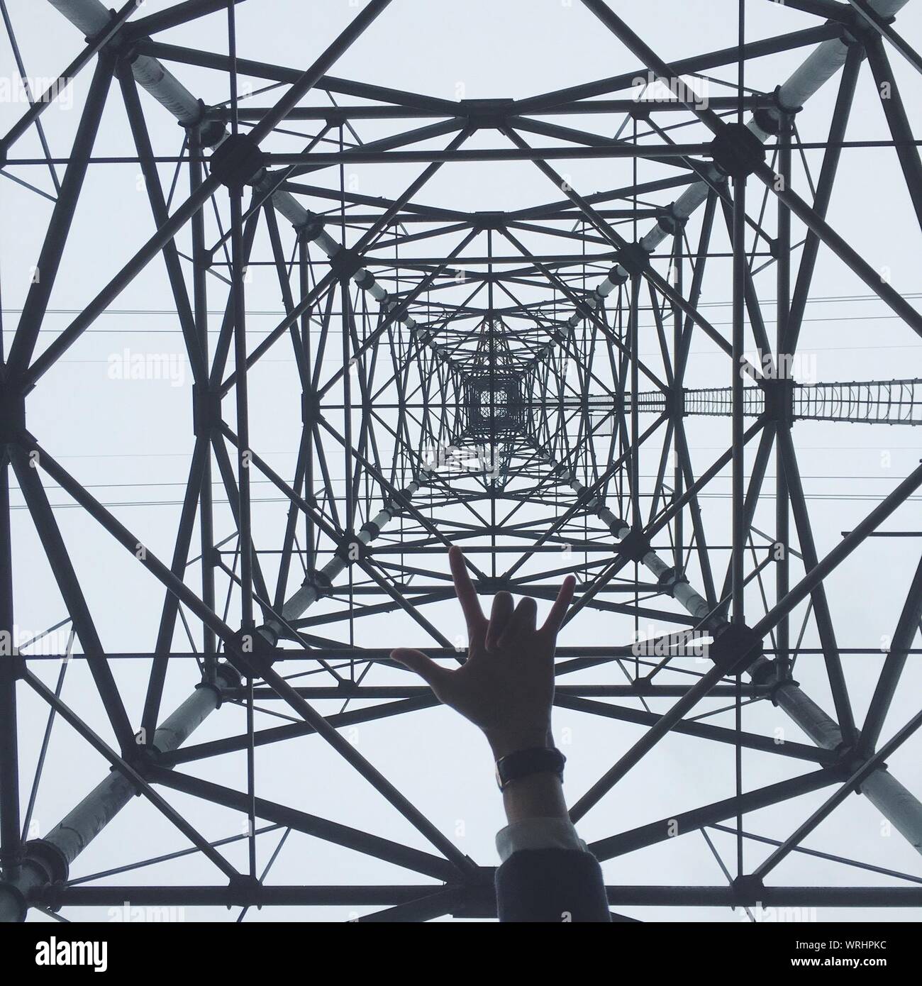 Cropped Hand Gesture Against Electricity Pylon Stock Photo