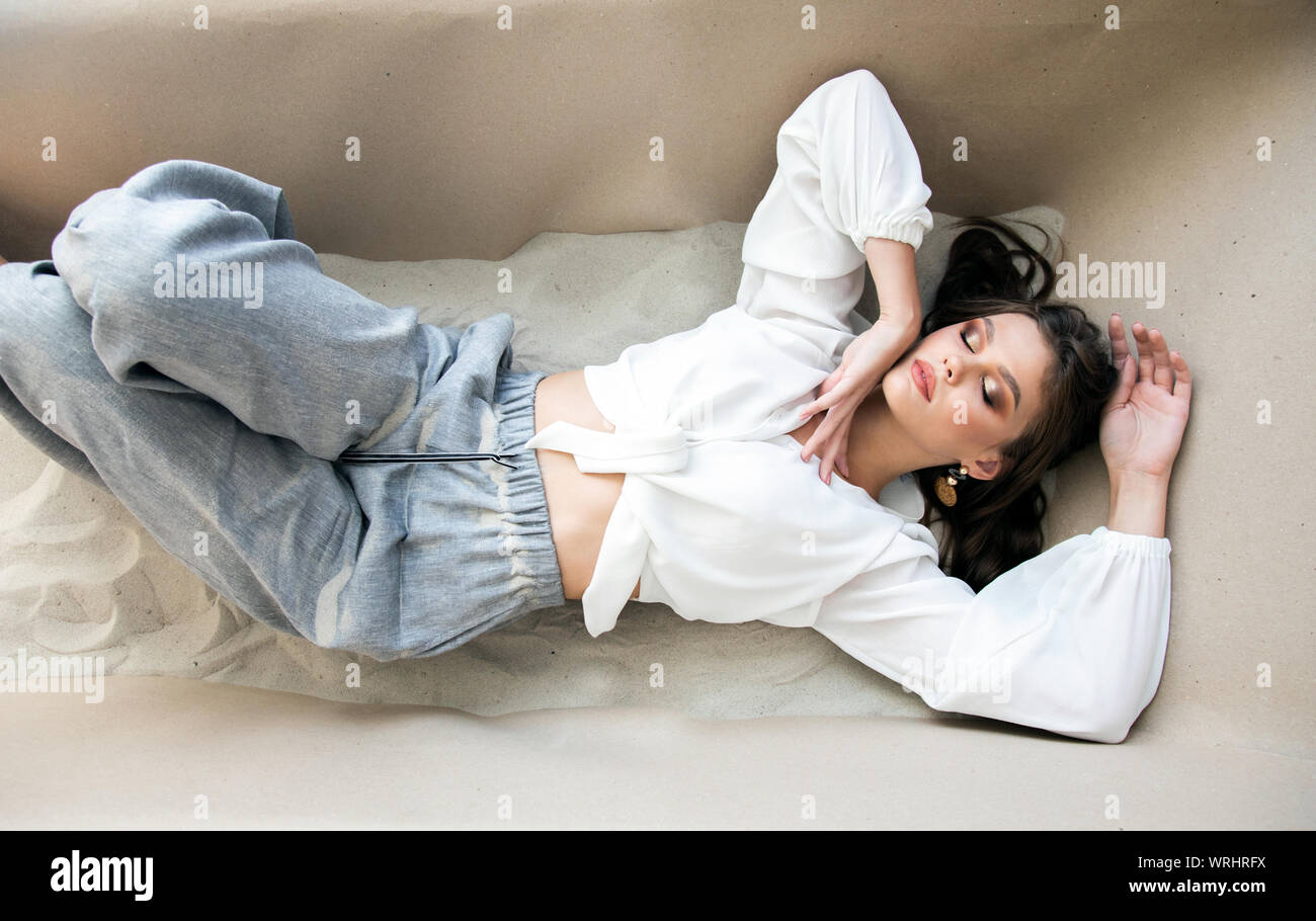 Dreaming cute brunette young girl lying in a bath of sand indoors Stock Photo