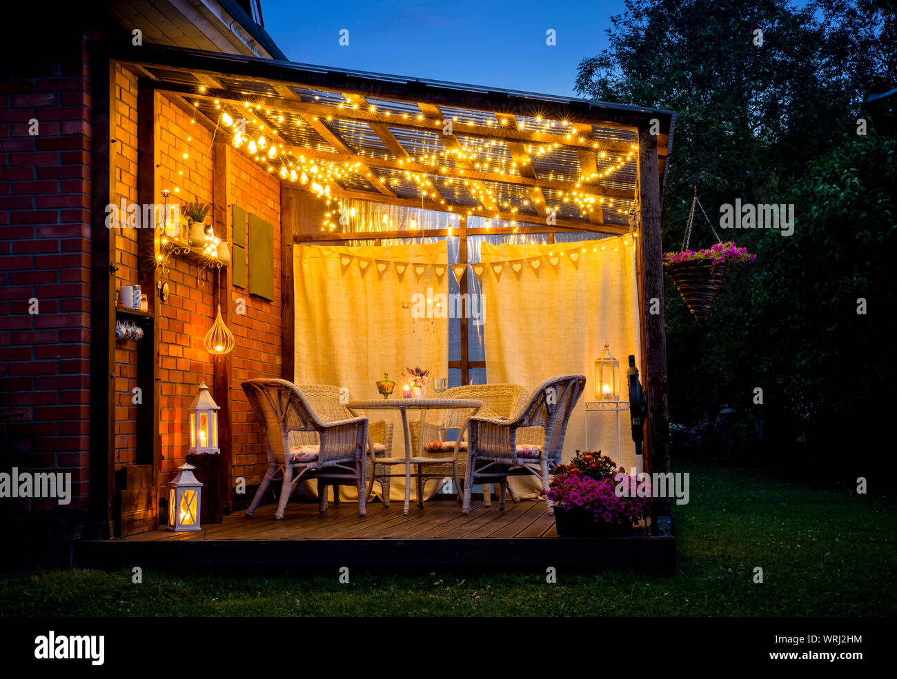 View over cozy outdoor terrace with table and chairs, very romantic lighting,  white lanterns, candles burning, led string party lights and bulbs with  Stock Photo - Alamy