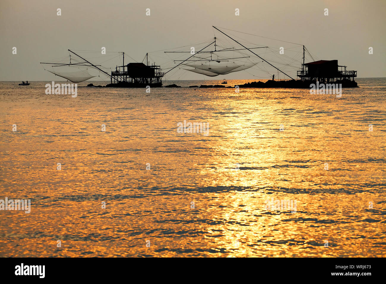 Silhouette Stilt Houses With Fishing Nets Amidst Sea Against Sky During Sunset Stock Photo