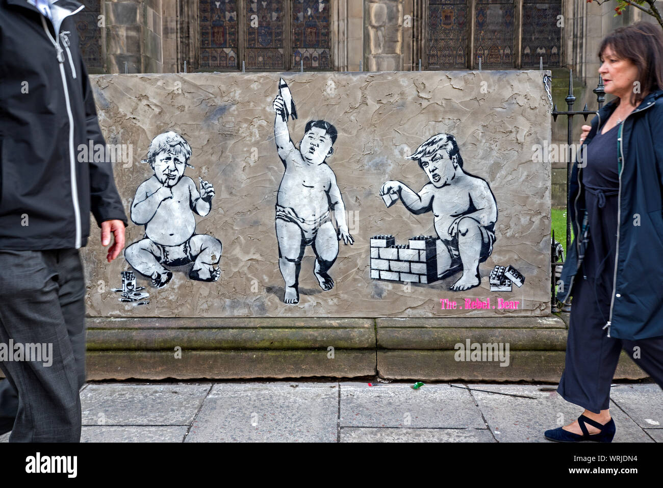 Pedestrians walking by piece of street art depicting Donald Trump, Boris Johnson and Kim Jong Un as babies playing with toys. Edinburgh, Scotland. Stock Photo