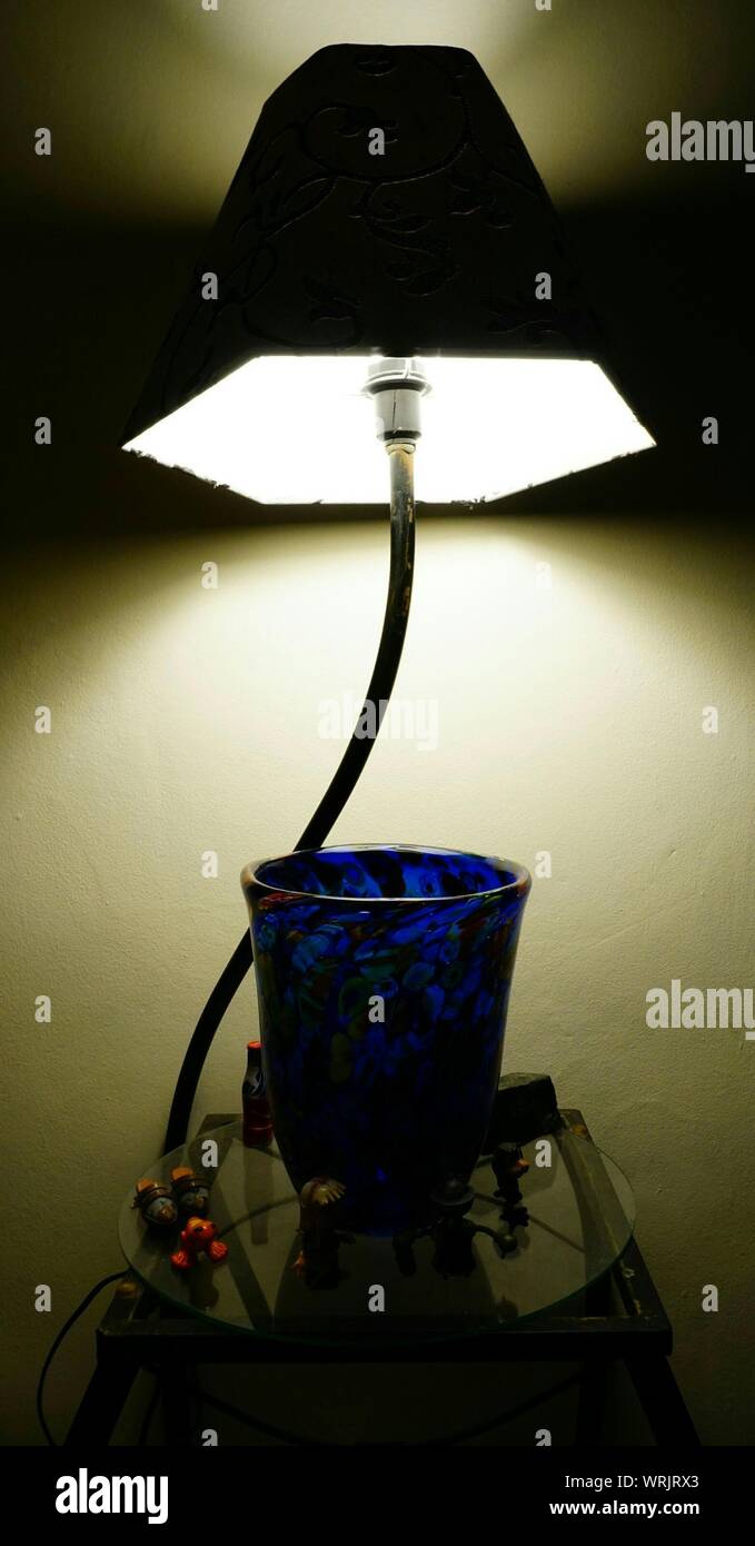 Close-up Of Illuminated Lamp Shade Over Porcelain Vase On Table Against Wall Stock Photo