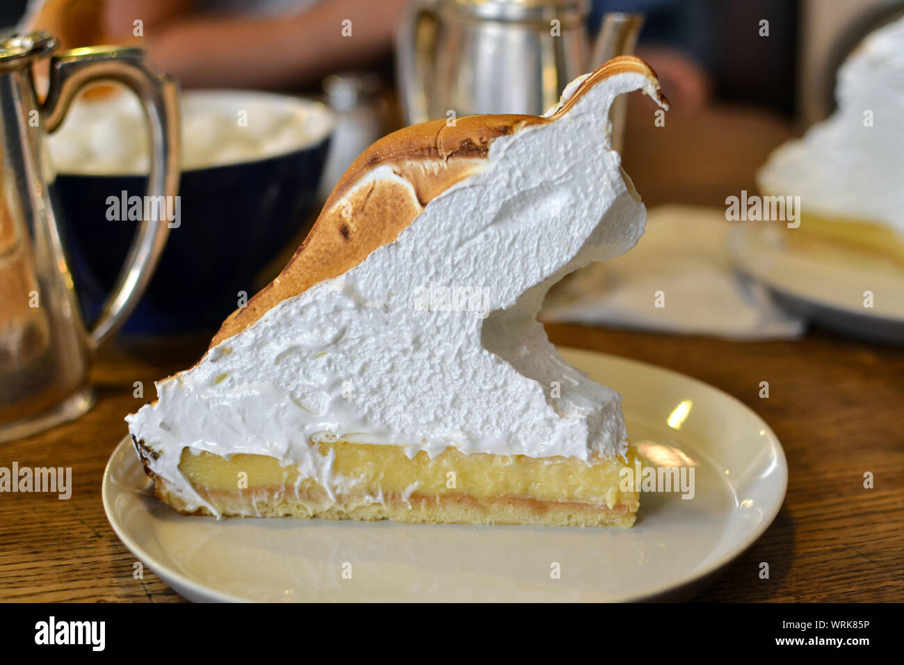 Gigantic piece of yummy lemon meringue pie on wooden table in a café. Stock Photo
