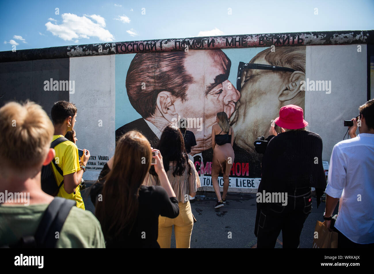 19 August 2019, Berlin: Tourists and visitors stand in front of the so-called 'Brother Kiss Painting' at the East Side Gallery. Almost 30 years ago, artists immortalized themselves here and reinterpreted the longest remaining section of the Berlin Wall with their works of art. Photo: Arne Immanuel Bänsch/dpa Stock Photo