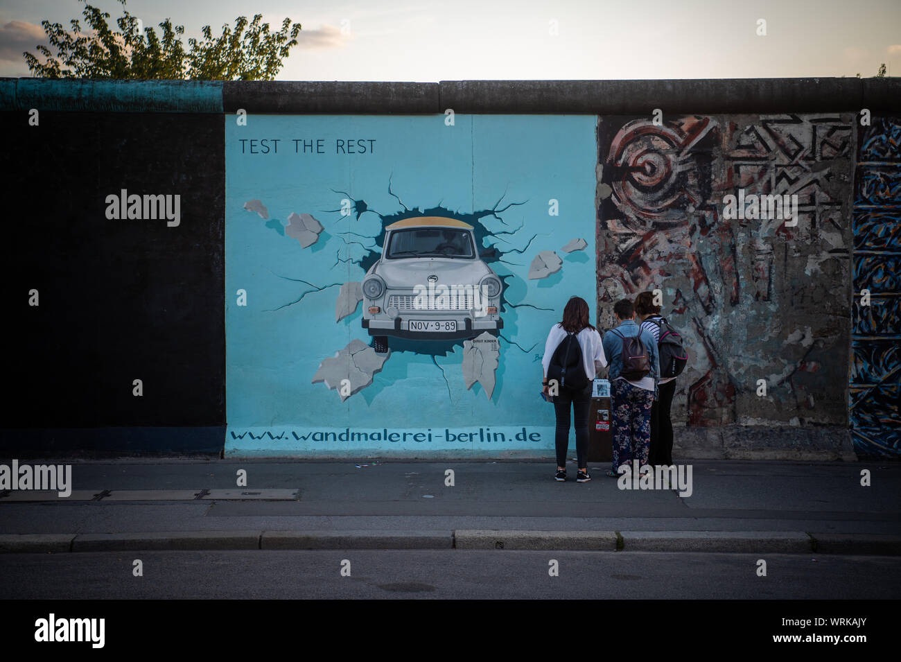 19 August 2019, Berlin: Visitors and tourists stand in front of the Trabi picture of the artist Birgit Kinder at the East Side Gallery. Almost 30 years ago, artists immortalized themselves here and reinterpreted the longest remaining section of the Berlin Wall with their works of art. Photo: Arne Immanuel Bänsch/dpa Stock Photo
