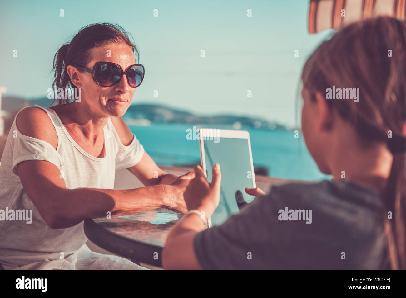 Mother and daughter sitting on balcony and using tablet Stock Photo