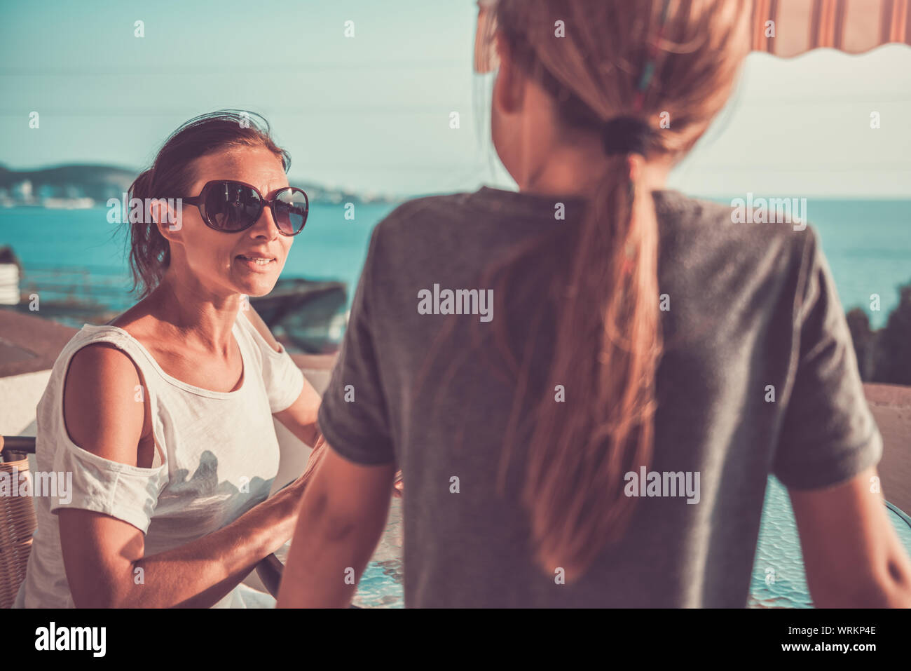 Mother wearing sunglasses talking with daughter on balcony Stock Photo