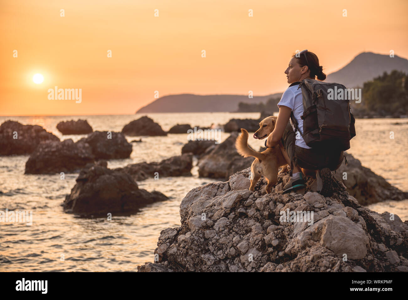 Woman with a dog hiking along the seashore during sunset Stock Photo