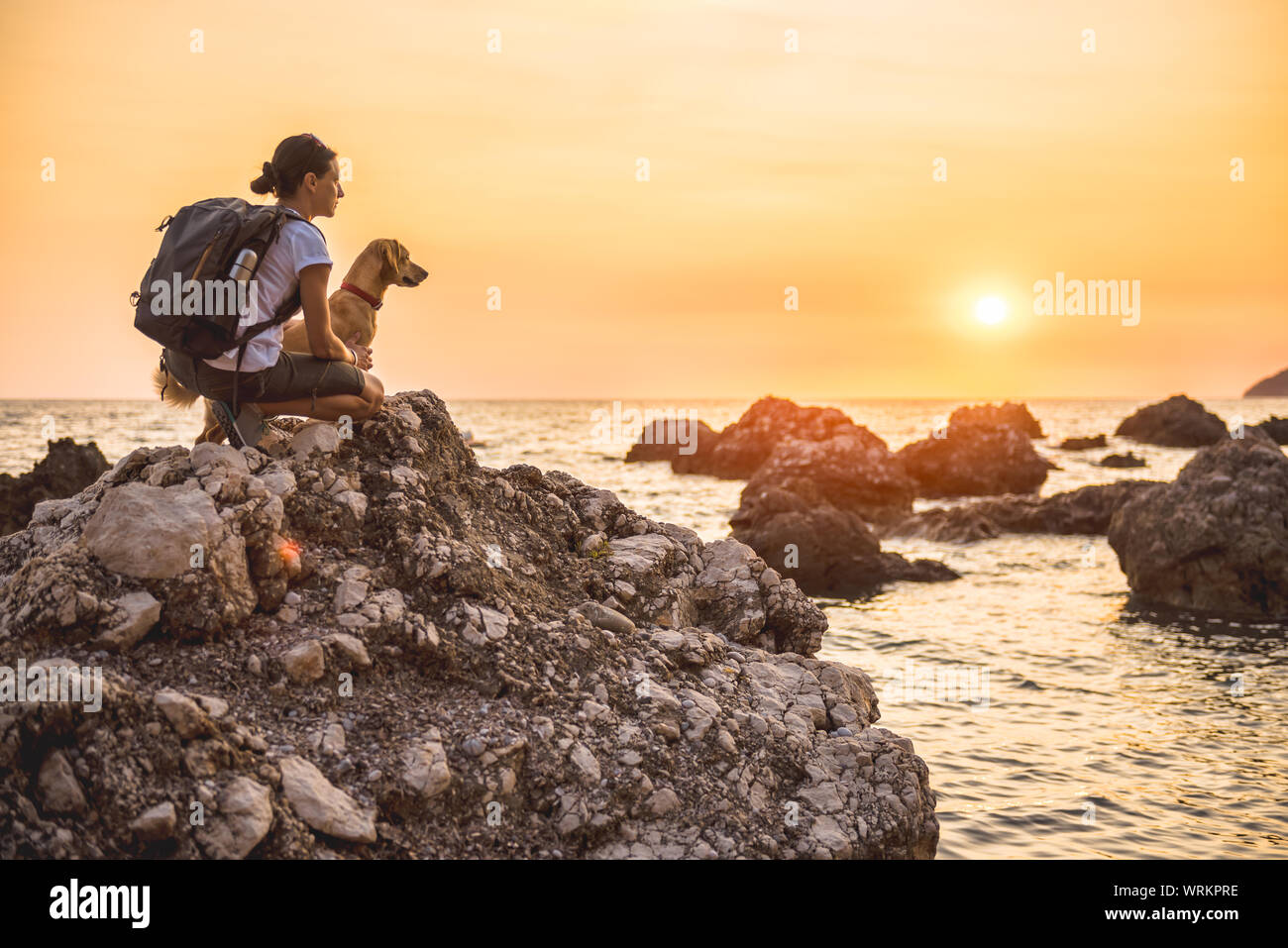 Woman with a dog hiking along the seashore during sunset Stock Photo