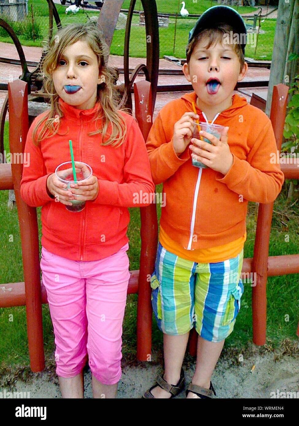 Siblings Eating Shaved Ice While Standing At Park Stock Photo