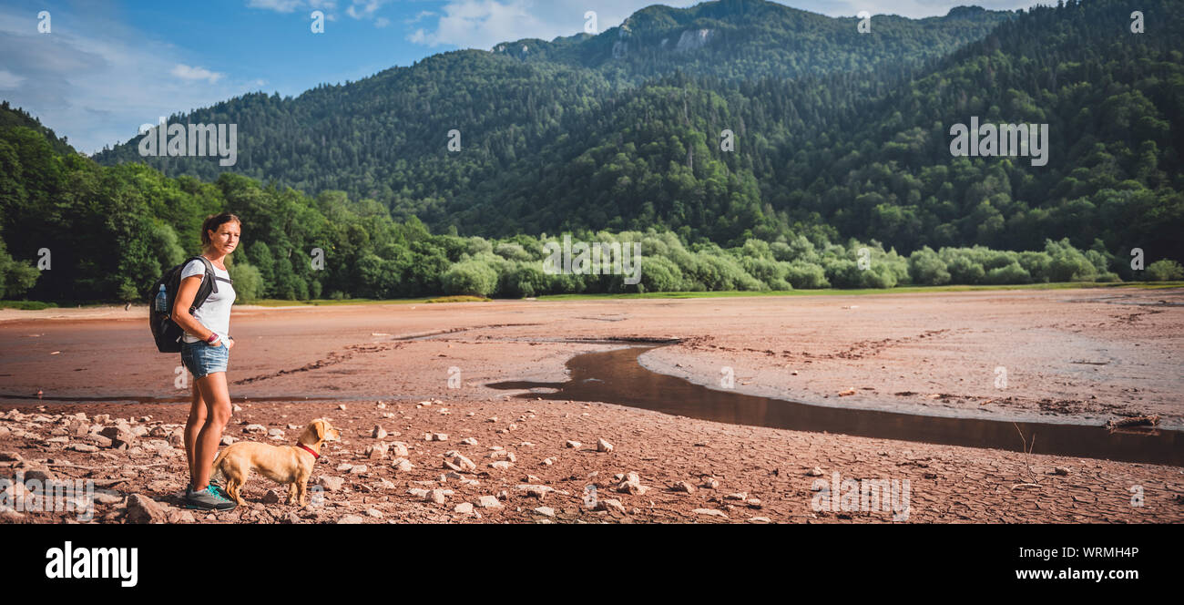 Female hiker with a dog standing on a dried mountain lake bed Stock Photo