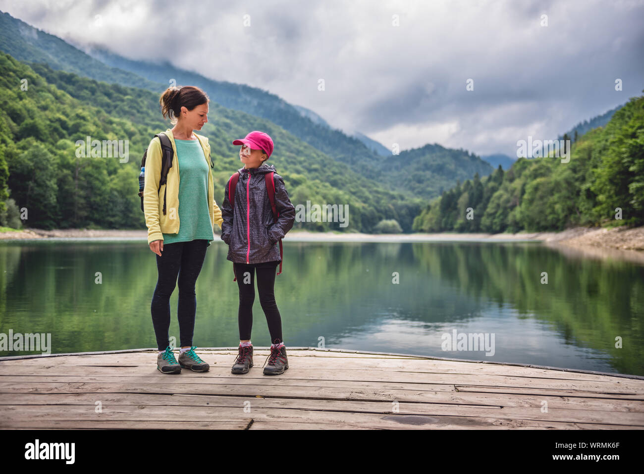 Mother and daughter standing on the pier by the mountain lake Stock Photo