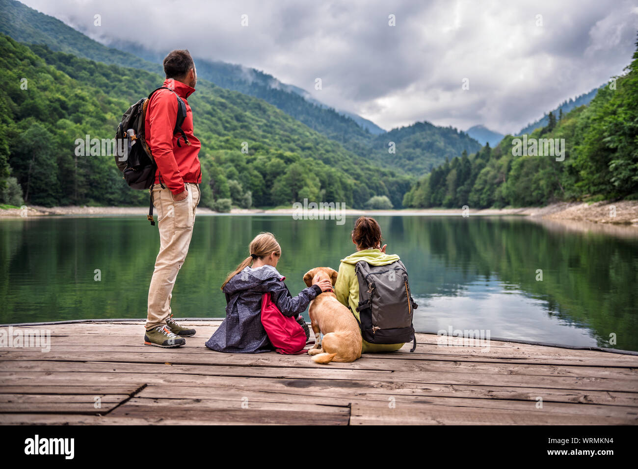 Family with small yellow dog resting on a pier and looking at lake and foggy mountains Stock Photo