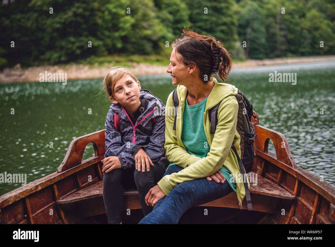 Mother and daughter sitting in a wooden boat on the mountain lake and talking Stock Photo