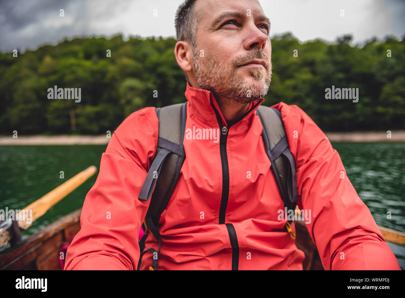 Man wearing red jacket enjoying boat ride on a mountain lake Stock Photo