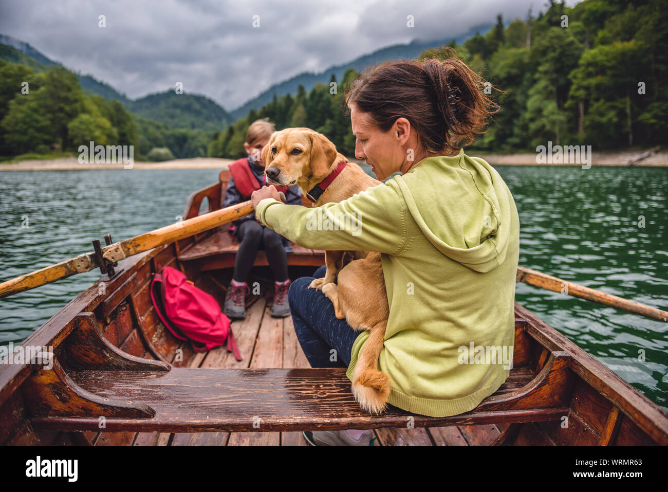 Mother and daughter with a small yellow dog rowing a boat on a mountain lake Stock Photo