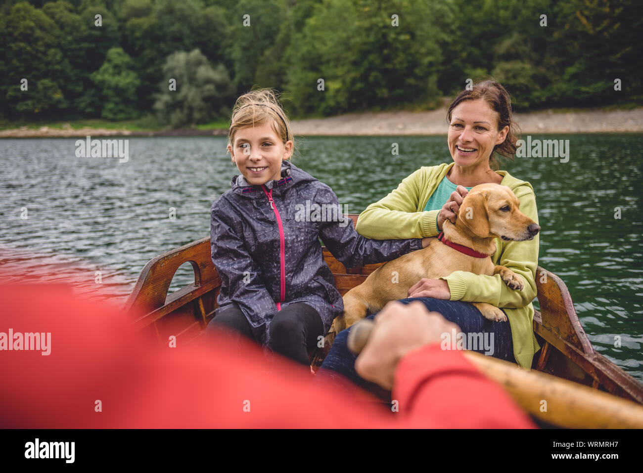 Family with small yellow dog rowing on the mountain lake in a boat