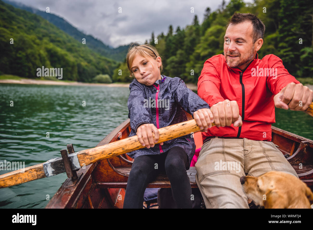 Father and daughter with a small yellow dog rowing a boat on a mountain lake Stock Photo