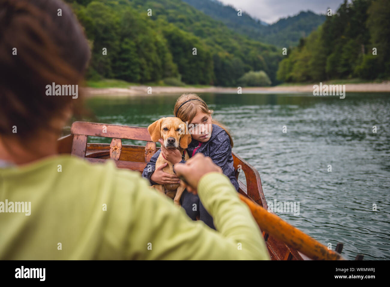 Mother and daughter with a small yellow dog rowing a boat on a mountain lake Stock Photo