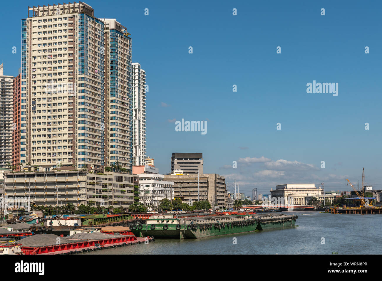 Manila, Philippines - March 5, 2019: Outside Fort Santiago. Barges and skyscrapers apartment buildings along Pasig River under blue sky. Central Posta Stock Photo