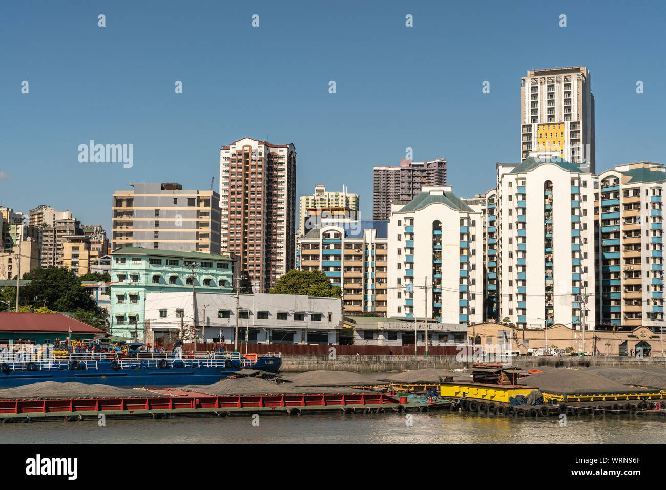 Manila, Philippines - March 5, 2019: Outside Fort Santiago. Barges and skyscrapers apartment buildings across Pasig River under blue sky. Stock Photo
