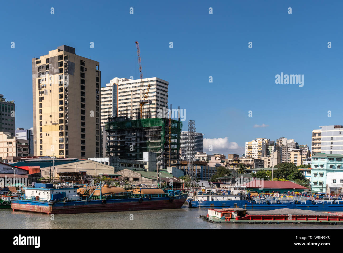 Manila, Philippines - March 5, 2019: Outside Fort Santiago. Barges and skyscrapers apartment buildings across Pasig River under blue sky. Tower under Stock Photo