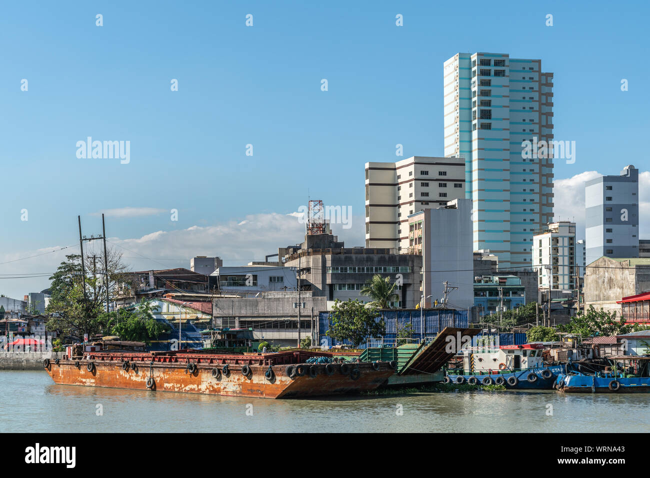 Manila, Philippines - March 5, 2019: Outside Fort Santiago. Barges and skyscrapers apartment buildings across Pasig River under blue sky. Stock Photo