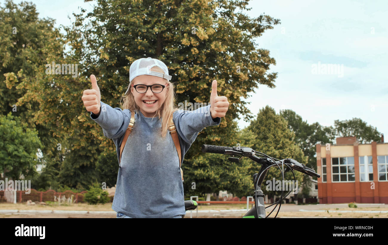 An 11 year old girl shows her thumbs up in a good mood next to her bicycle in the summer. Stock Photo