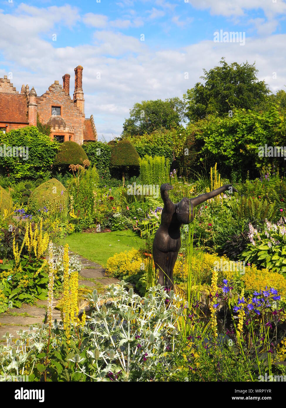 Portrait of Chenies Manor house and sunken garden, ornamental pond with Alan Biggs' sculpture;f resh green plant border in late afternoon sun in June. Stock Photo