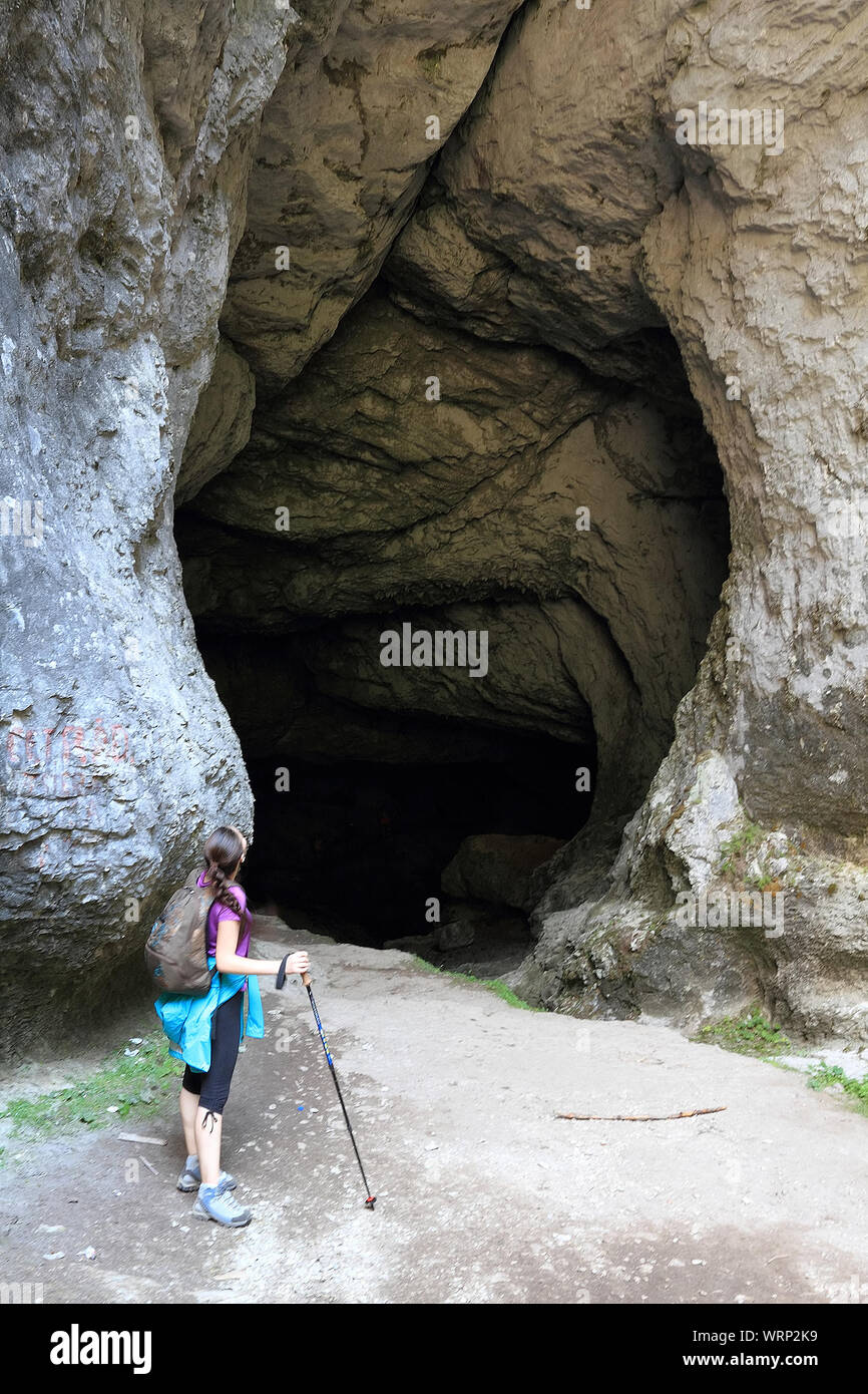 Woman With Hiking Pole Standing At Entrance Of Cave Stock Photo