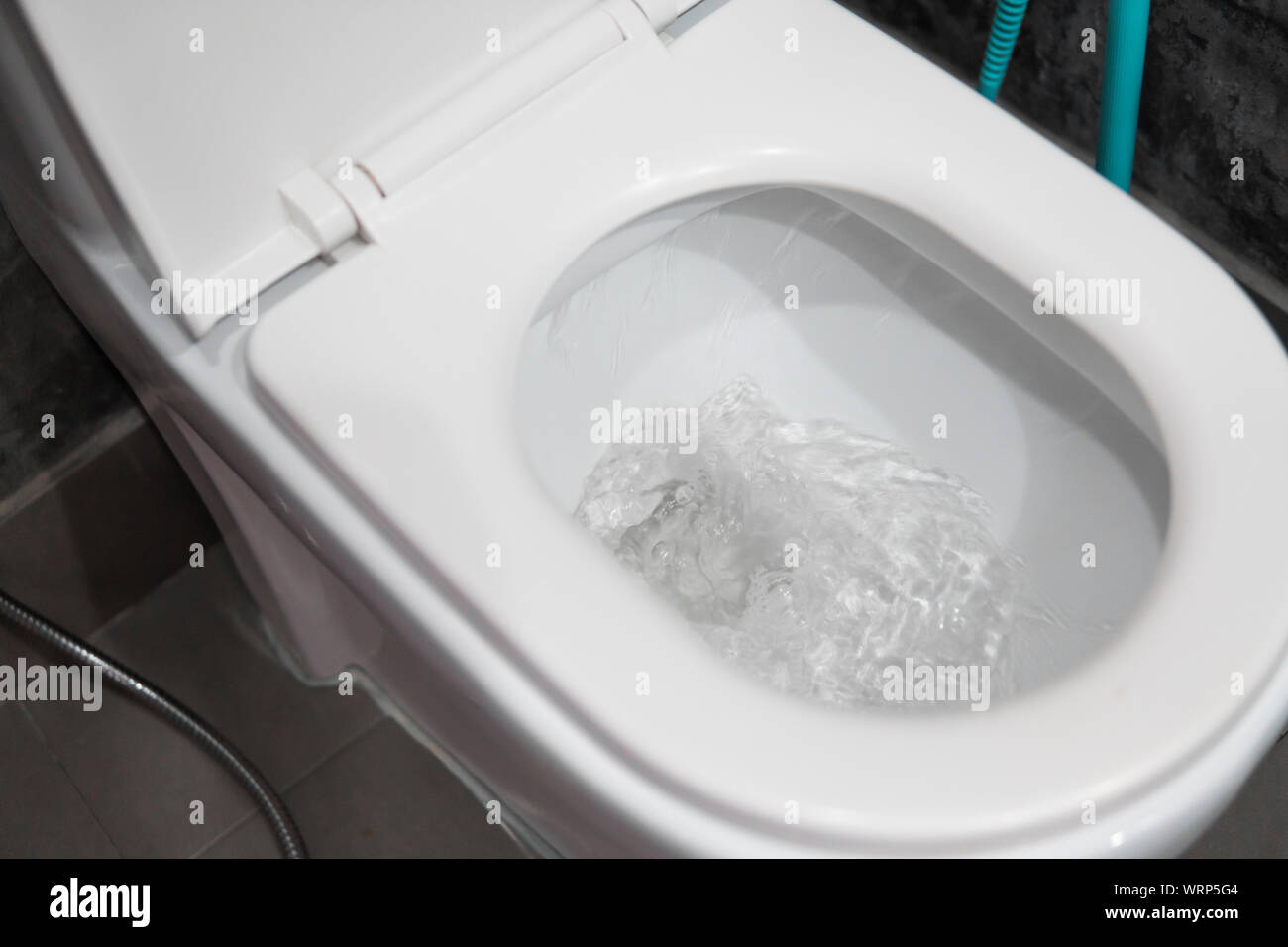 Water flushing in toilet bowl. White hanging toilet seat on white