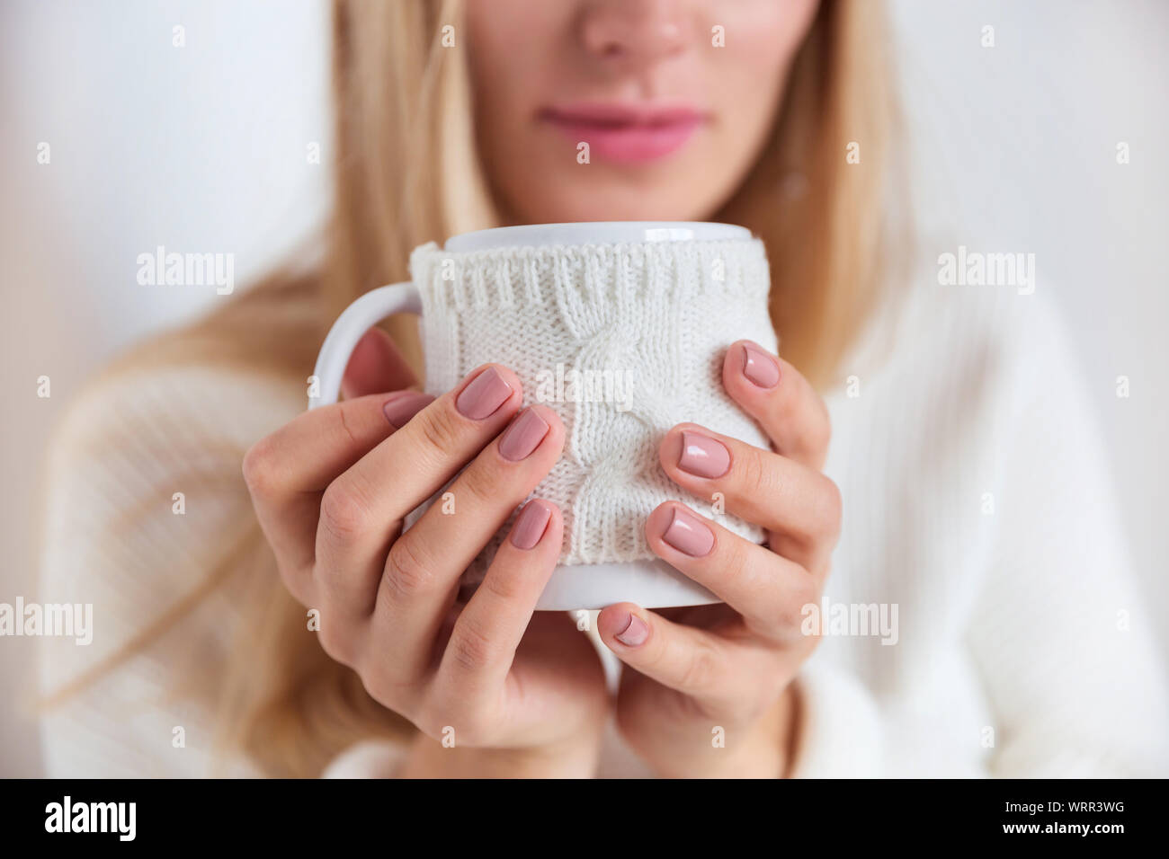 Close-up of a blond girl in a white sweater with a cup of hot tea in her hands Stock Photo