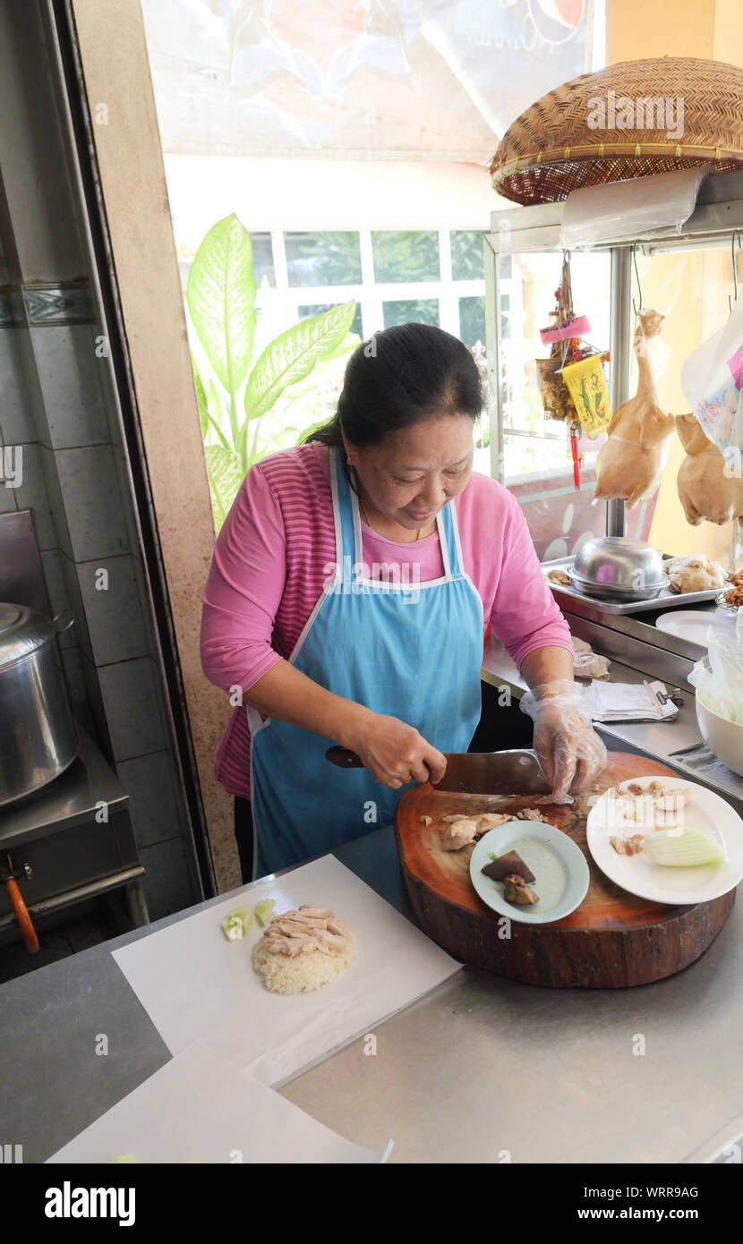 Middle-aged Asian women chopped boiled chicken meat on a wooden chopping board, Cooking for sale in the chicken rice shop in Thailand Stock Photo