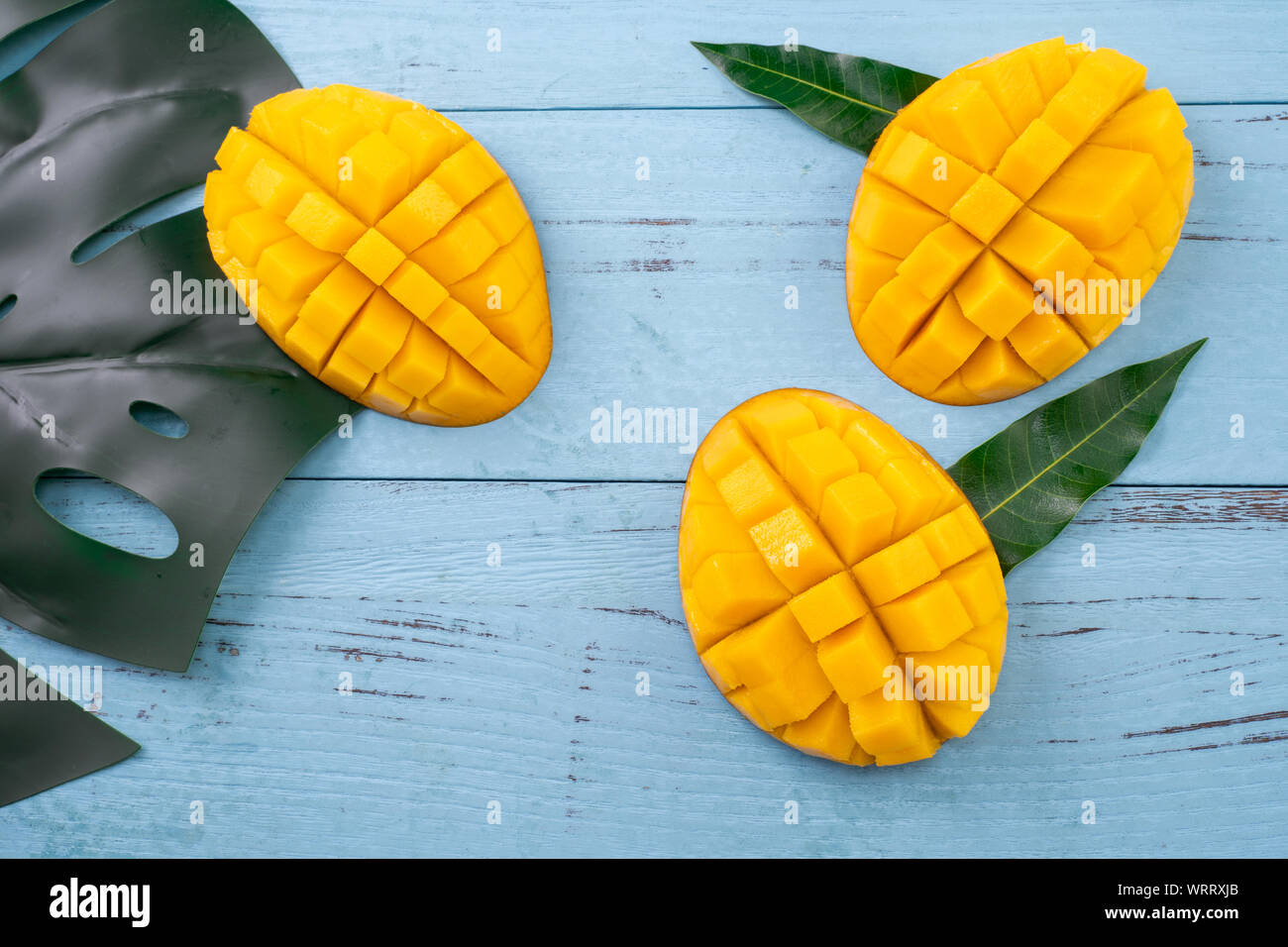 Fresh mango, beautiful chopped fruit with green leaves on dark wooden ...
