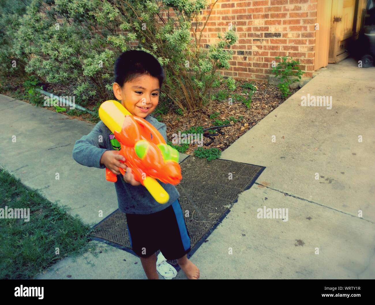High Angle View Of Boy Squirting Water From Gun In Back Yard Stock Photo