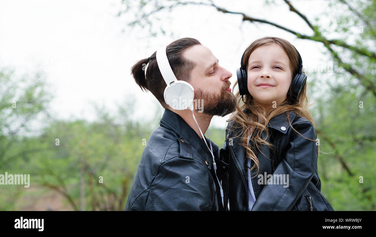 Fashionable stylish family for a walk. Charming schoolchild and her handsome young dad in headphones are listening to music. Time together. Family loo Stock Photo