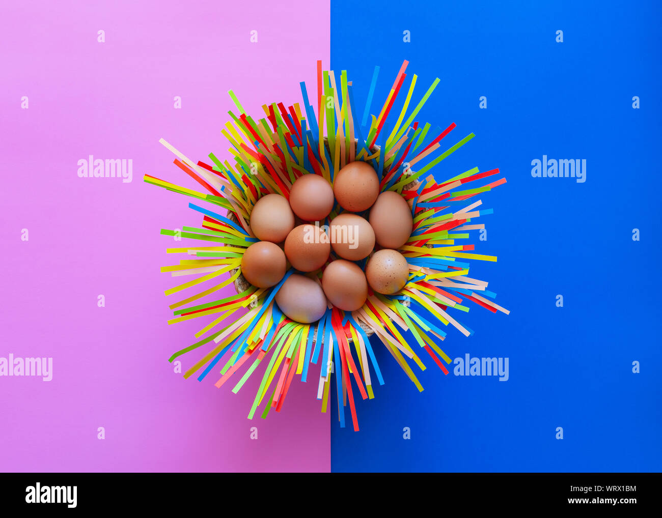 Chicken eggs in a basket on pink and blue paper background, Easter eggs concept. Stock Photo