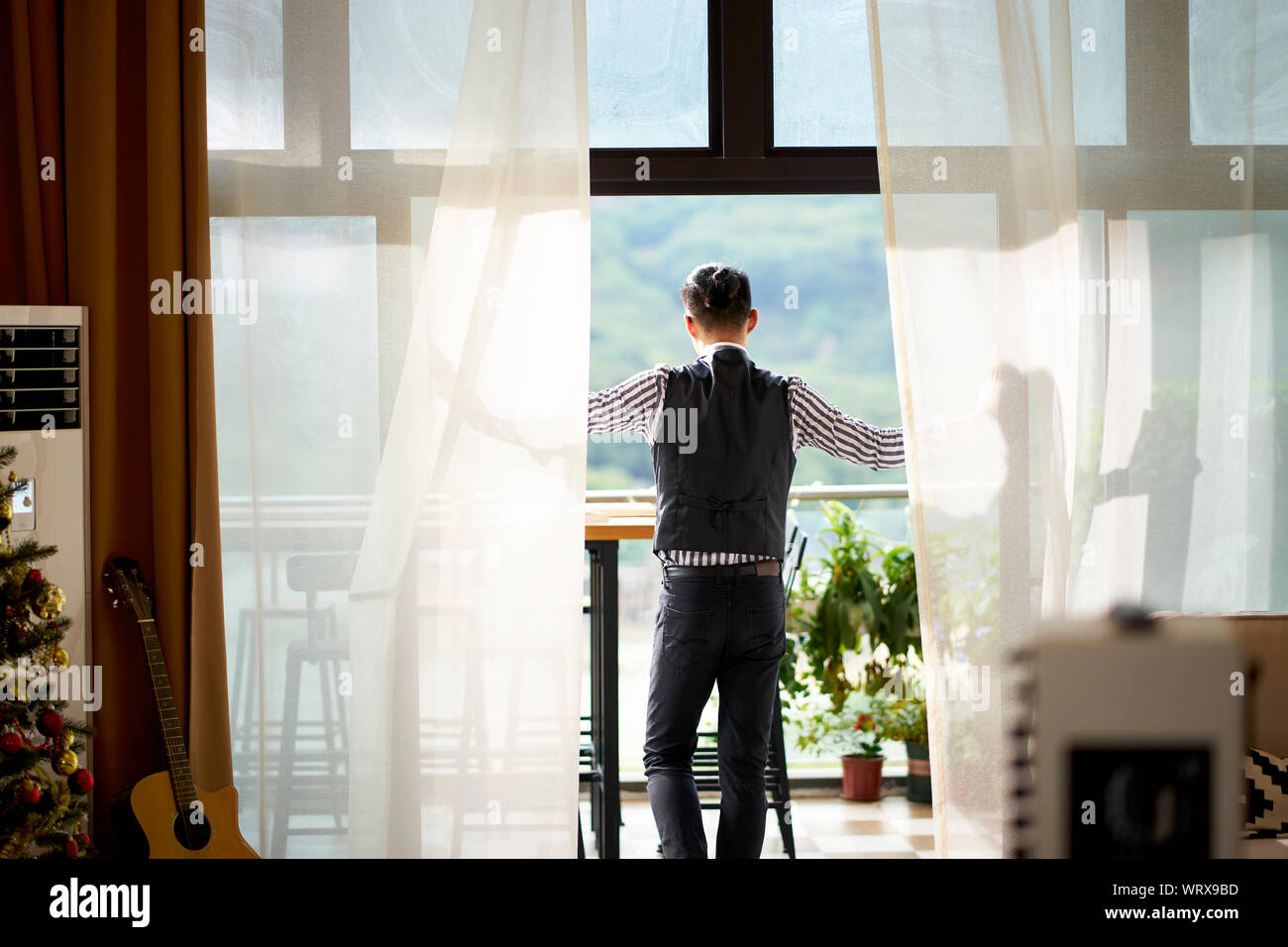 young asian man standing on patio looking at mountain view Stock Photo