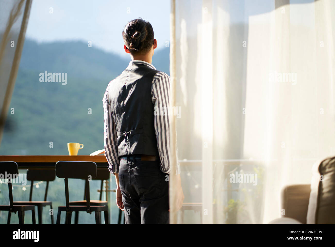 young asian man standing on patio looking at mountain view Stock Photo