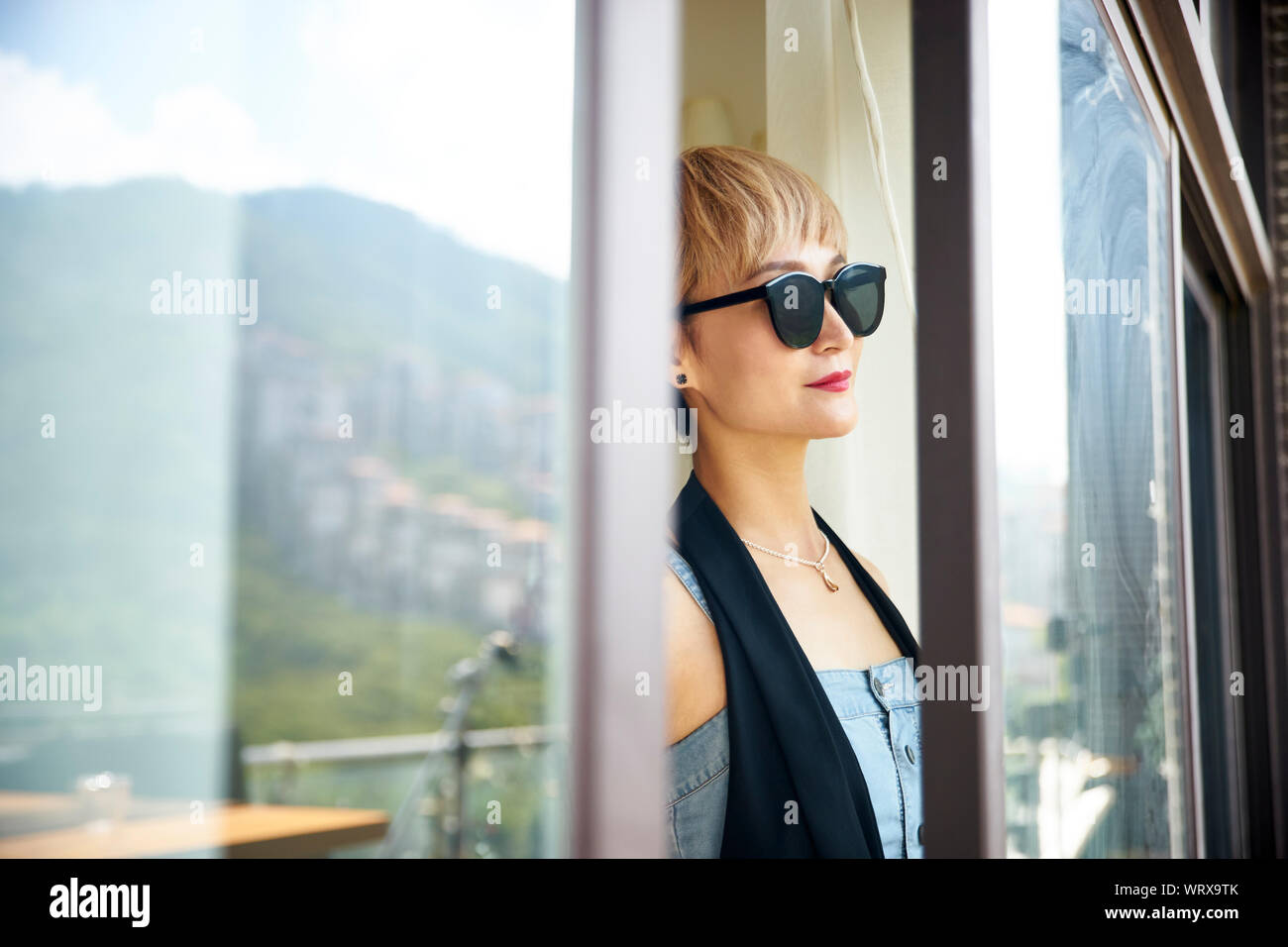 asian woman wearing sunglasses looking at view by the window Stock Photo