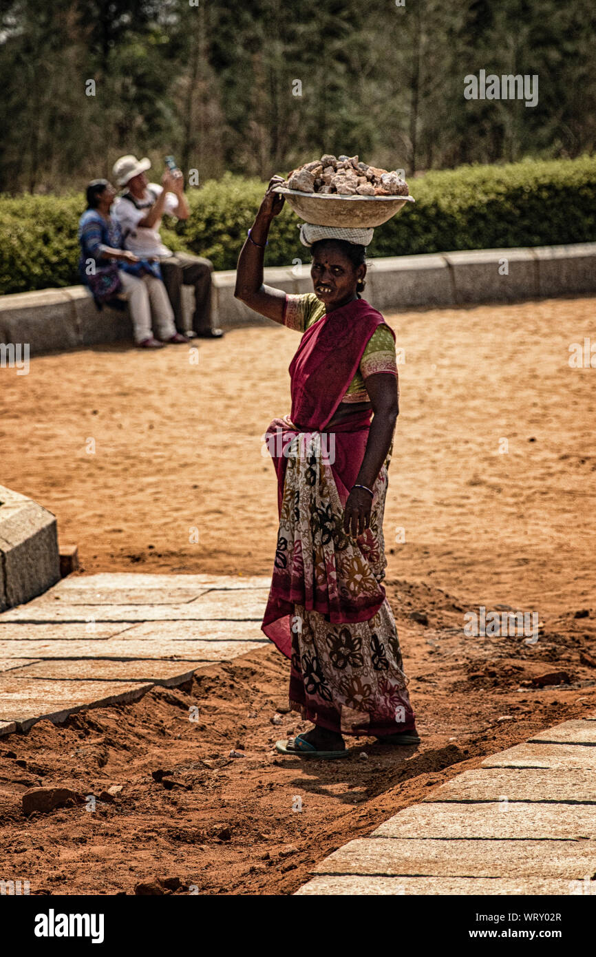 Indian woman in colorful saree carrying rocks in a basket on her head at Shore Temple, Mahabalipuram, India Stock Photo