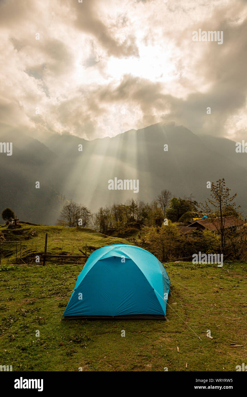 Morning sun rays fall on a blue tent at the camping site of Tshoka on the trekking route to Gochela pass in the Kanchenjunga mountain range in India Stock Photo