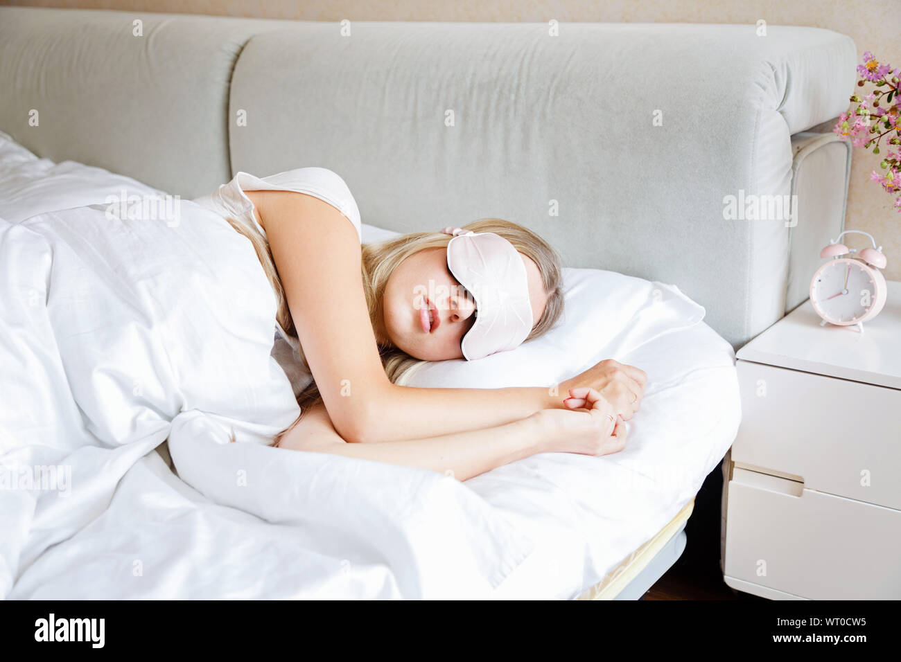 Young woman with long blonde hair sleeps on comfortable bed in a mask