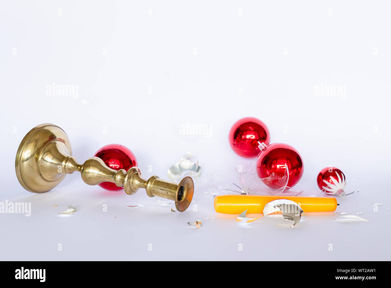 Front view of falling and shattered red and silver Christmas baubles and a bronze candleholder with a yellow candle on white background Stock Photo