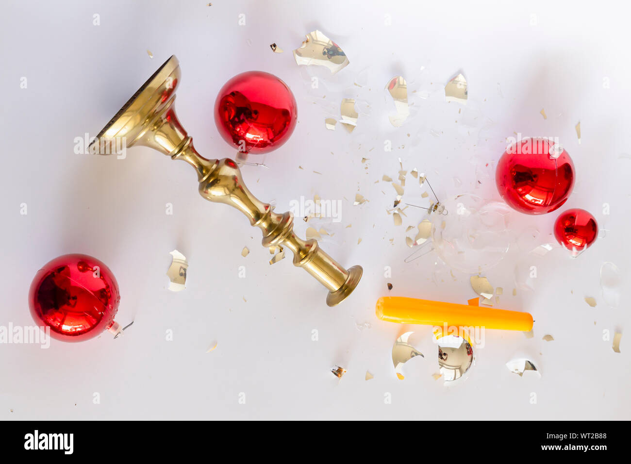 Top view of shattered red and silver Christmas baubles and an overturned bronze candleholder with a yellow candle on white background Stock Photo