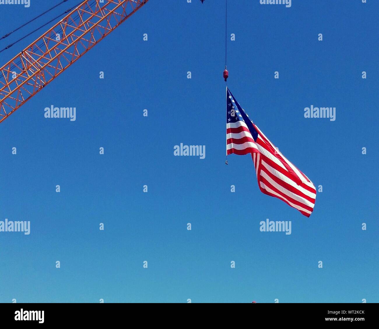 Low Angle View Of American Flag Hanging On Crane Against Clear Blue Sky Stock Photo