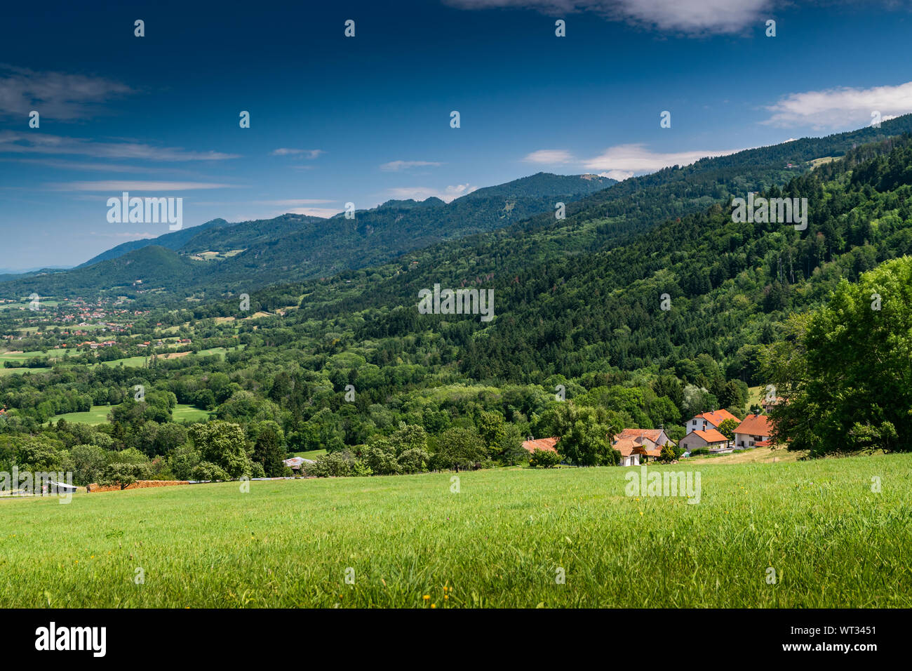 Mountain hill landscape overgrown with forests and country houses with blue sky,focus area on country houses.Haute-Savoie in France. Stock Photo